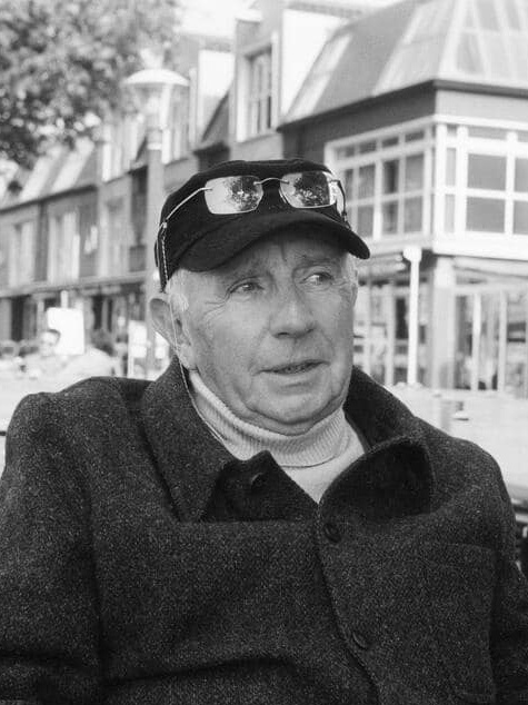 Portrait en noir et blanc de Paul Virilio, assis en terrasse dans un environnement urbain.