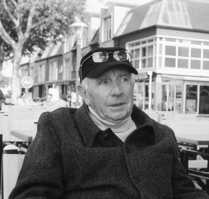 Portrait en noir et blanc de Paul Virilio, assis en terrasse dans un environnement urbain.